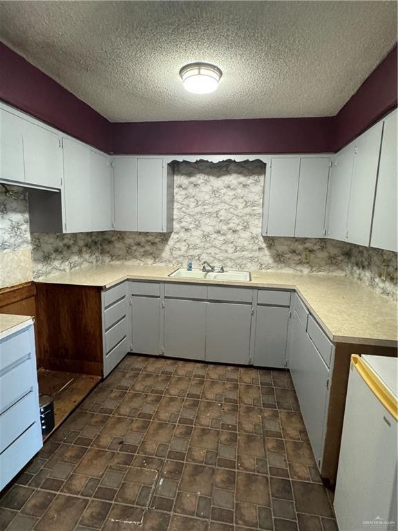 kitchen with tasteful backsplash, sink, white cabinets, and a textured ceiling