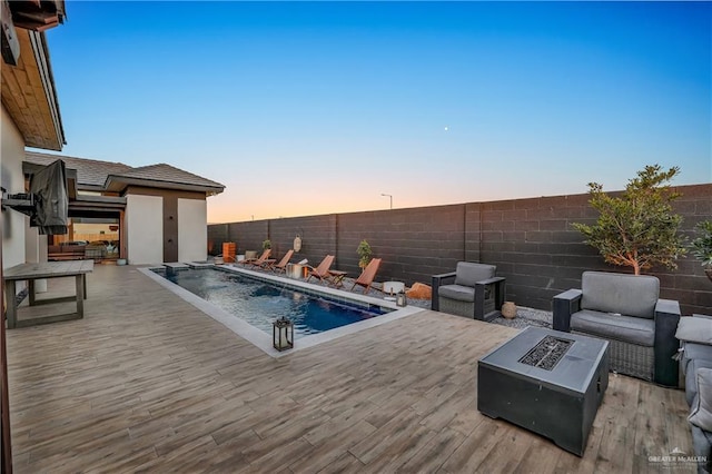 pool at dusk featuring an outdoor living space with a fire pit, pool water feature, and a deck