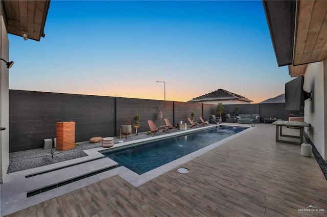 pool at dusk featuring pool water feature and a deck