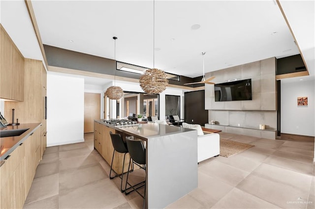 kitchen with sink, hanging light fixtures, light brown cabinets, a large island with sink, and a kitchen breakfast bar