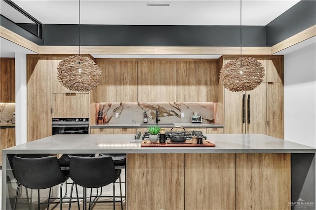 kitchen featuring pendant lighting, black oven, sink, a breakfast bar area, and stainless steel gas cooktop