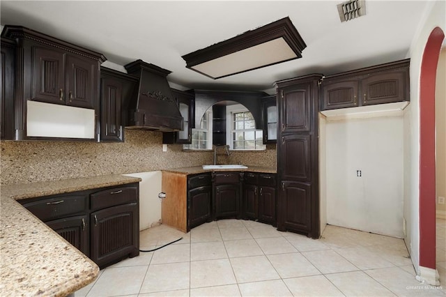 kitchen featuring arched walkways, premium range hood, backsplash, and a sink