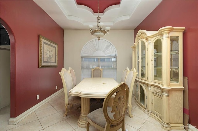 dining space with light tile patterned floors, baseboards, arched walkways, a tray ceiling, and a chandelier