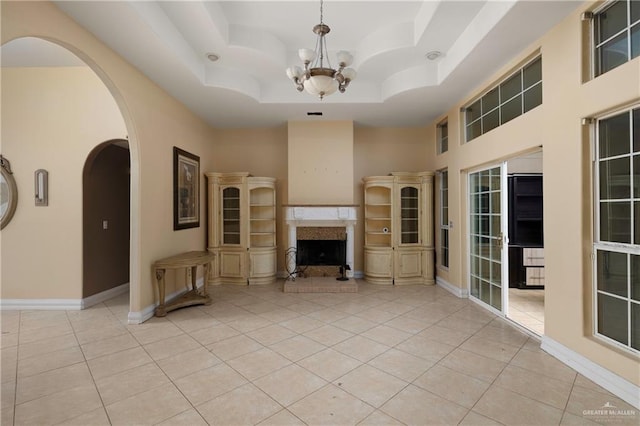 unfurnished living room with light tile patterned floors, baseboards, a raised ceiling, and a fireplace with raised hearth