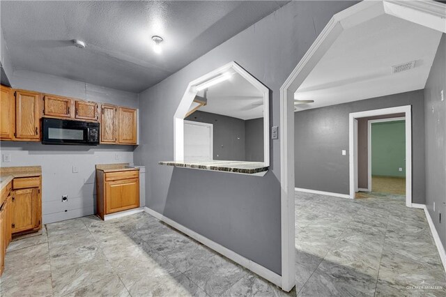 1619 Beech Ave, Mercedes, TX 78570 - kitchen with black microwave, brown cabinets, baseboards, light countertops, and a textured ceiling