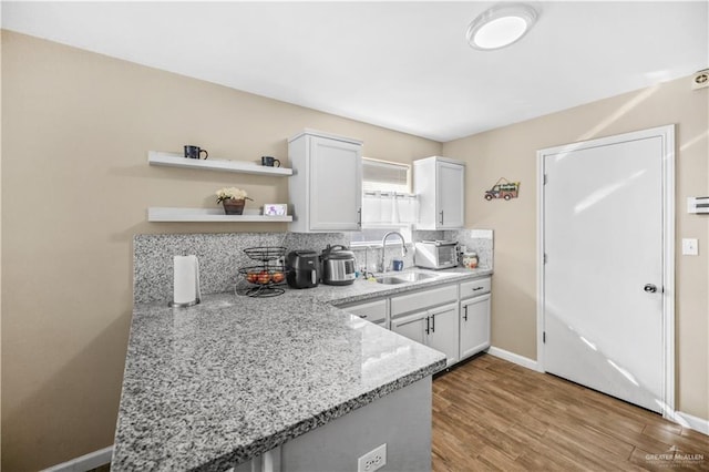 kitchen with a sink, light stone countertops, decorative backsplash, wood finished floors, and open shelves