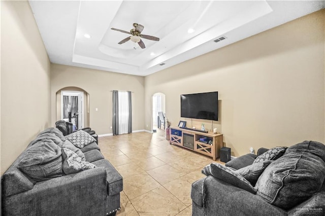 living room featuring a tray ceiling, arched walkways, visible vents, and ceiling fan