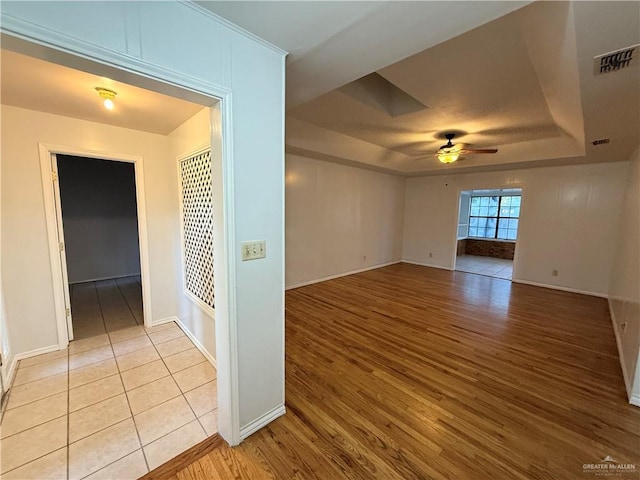 empty room featuring ceiling fan, a raised ceiling, and light hardwood / wood-style flooring