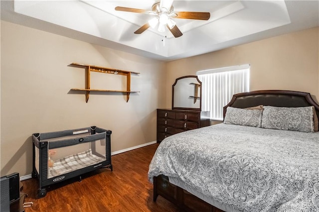 bedroom featuring ceiling fan, dark wood-type flooring, and a tray ceiling