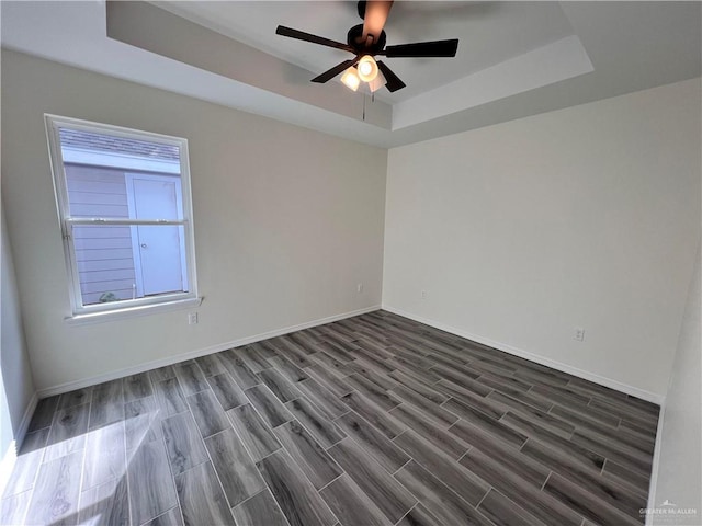 unfurnished room with dark hardwood / wood-style flooring, a tray ceiling, and ceiling fan