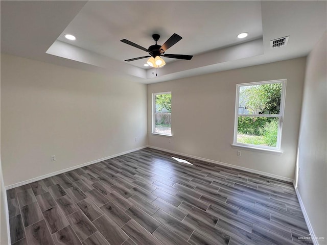 empty room with a wealth of natural light, ceiling fan, and a tray ceiling