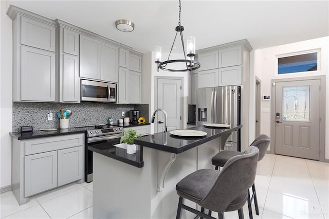 kitchen with gray cabinetry, decorative backsplash, a kitchen island with sink, and appliances with stainless steel finishes