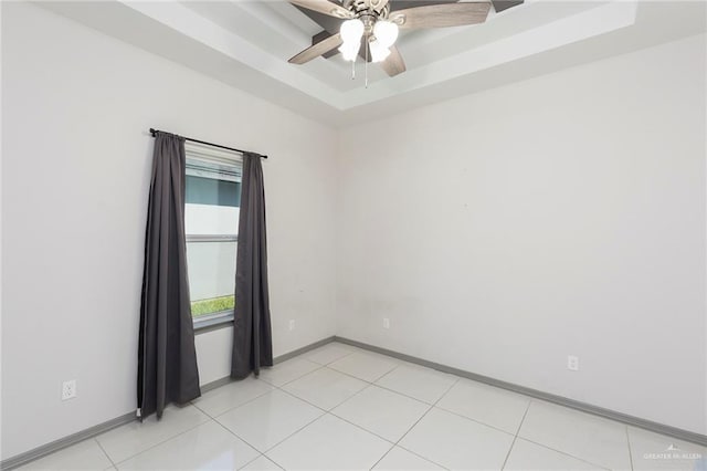 tiled empty room featuring a tray ceiling and ceiling fan