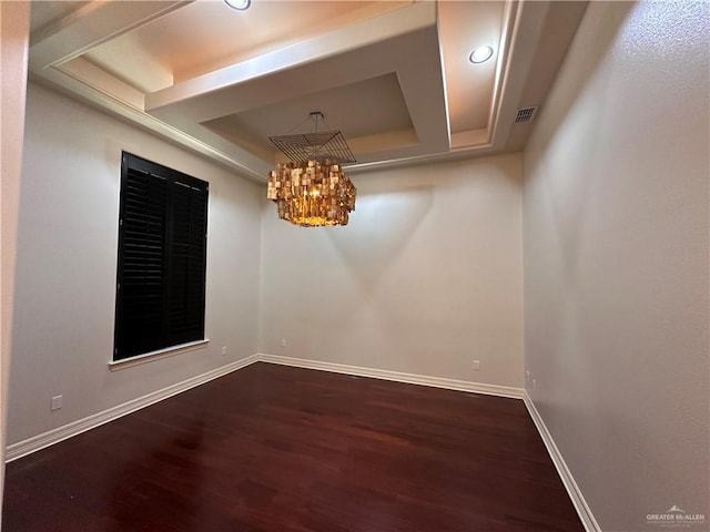 spare room with a chandelier, a raised ceiling, and dark wood-type flooring