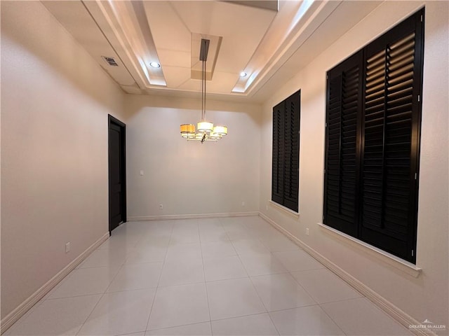 tiled spare room with a raised ceiling and an inviting chandelier