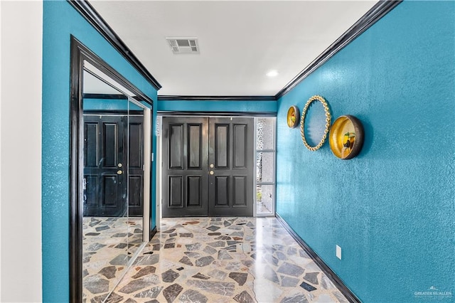 foyer entrance with a textured wall, visible vents, ornamental molding, and stone finish floor