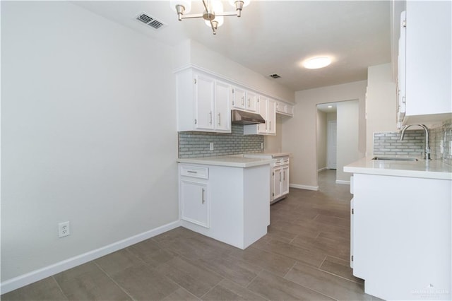 kitchen featuring backsplash, an inviting chandelier, white cabinetry, and sink