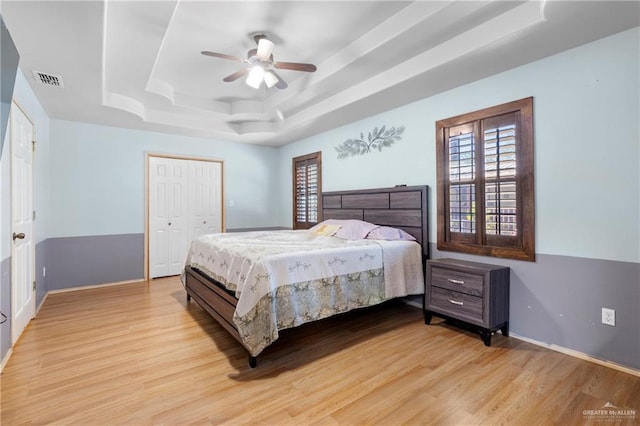 bedroom featuring light wood-type flooring, ceiling fan, a closet, and a tray ceiling