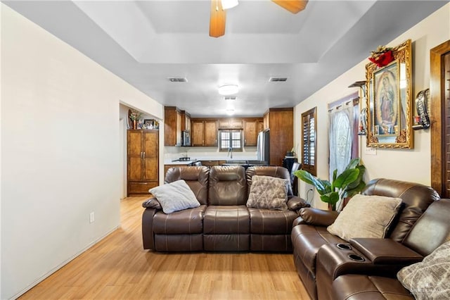 living room featuring ceiling fan, a raised ceiling, light hardwood / wood-style flooring, and sink