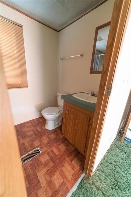 bathroom with vanity, toilet, parquet flooring, and a textured ceiling