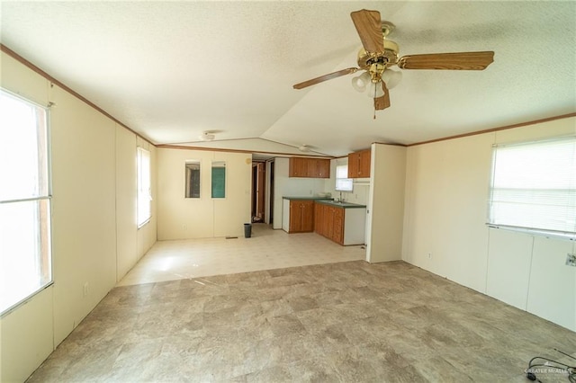 unfurnished living room with a textured ceiling, vaulted ceiling, a wealth of natural light, and ceiling fan