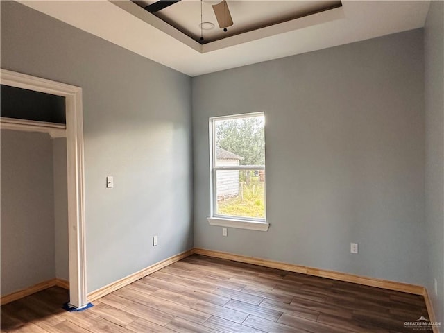 unfurnished bedroom with a raised ceiling, ceiling fan, a closet, and light hardwood / wood-style floors