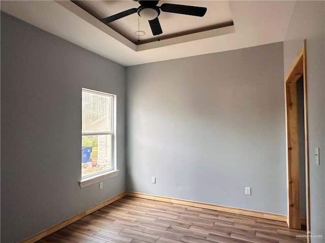 spare room with a raised ceiling, ceiling fan, and light hardwood / wood-style floors