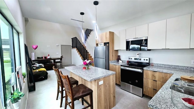 kitchen with a breakfast bar, decorative light fixtures, a kitchen island, appliances with stainless steel finishes, and white cabinets