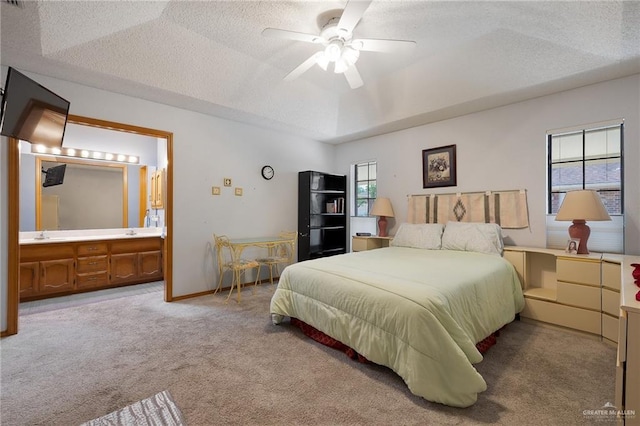 carpeted bedroom with ceiling fan, ensuite bath, a raised ceiling, and a textured ceiling