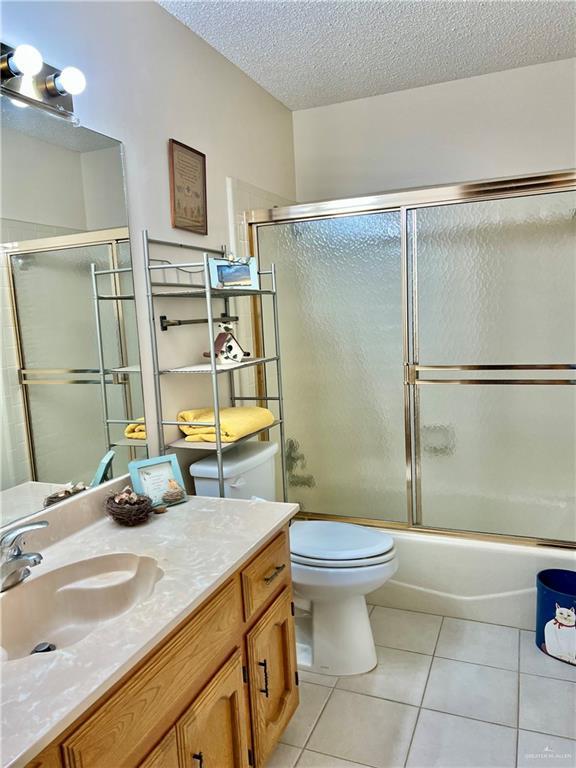 full bathroom with combined bath / shower with glass door, vanity, toilet, tile patterned floors, and a textured ceiling