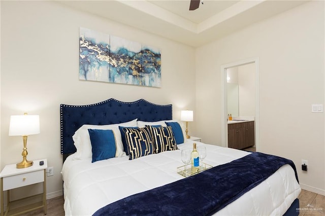 bedroom featuring ceiling fan, ensuite bath, a tray ceiling, and light hardwood / wood-style flooring