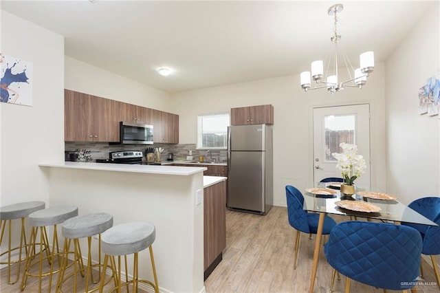 kitchen featuring a kitchen bar, tasteful backsplash, hanging light fixtures, appliances with stainless steel finishes, and kitchen peninsula