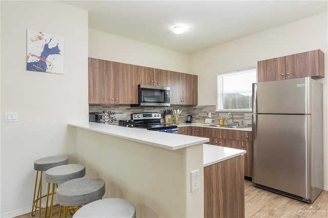 kitchen with a breakfast bar, sink, backsplash, kitchen peninsula, and stainless steel appliances