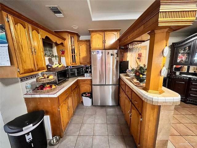 3300 Pradera St, Mission, TX 78574 - kitchen with freestanding refrigerator, tile countertops, brown cabinetry, light tile patterned flooring, and a peninsula