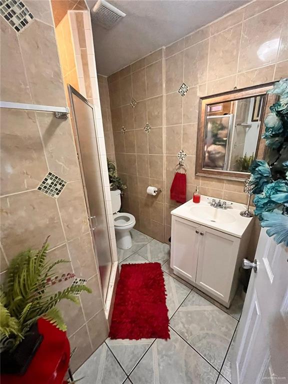 3300 Pradera St, Mission, TX 78574 - full bath with tile walls, vanity, a shower stall, tile patterned flooring, and toilet