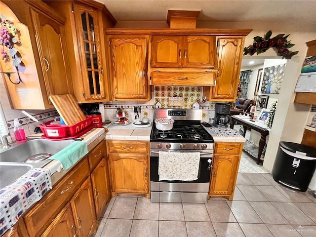 3300 Pradera St, Mission, TX 78574 - kitchen featuring gas stove, tile countertops, brown cabinetry, light tile patterned floors, and decorative backsplash