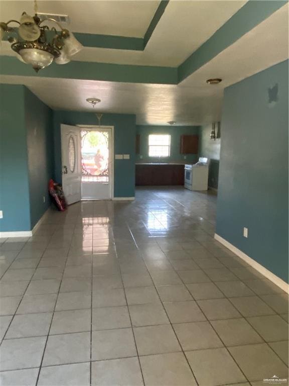 tiled empty room with a tray ceiling and a chandelier