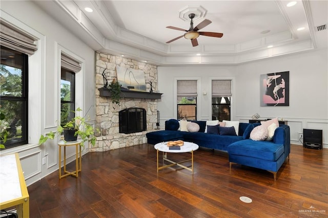 living room with a tray ceiling, a stone fireplace, dark hardwood / wood-style floors, and ceiling fan