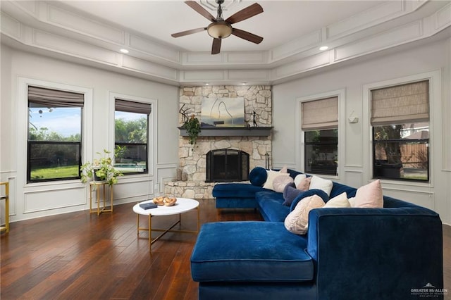 living room featuring ceiling fan, a stone fireplace, and dark hardwood / wood-style flooring