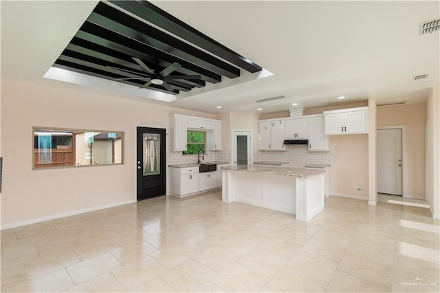 kitchen with a center island, sink, tasteful backsplash, light stone counters, and white cabinets