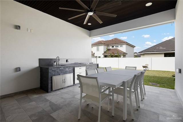 view of patio with a ceiling fan, outdoor dining space, a sink, exterior kitchen, and a fenced backyard