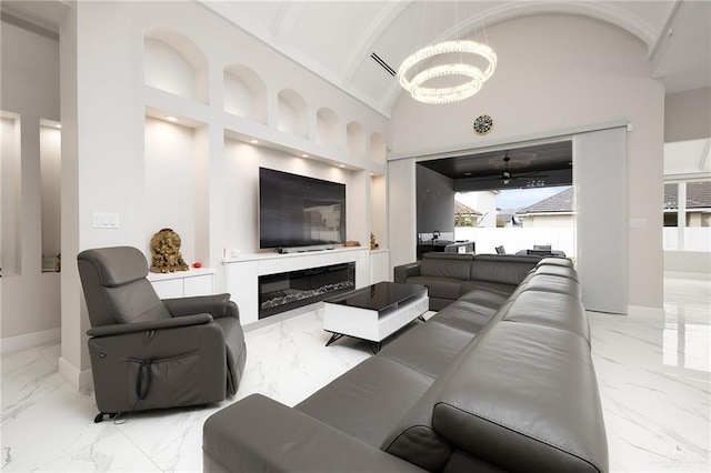 living room with marble finish floor, baseboards, an inviting chandelier, a glass covered fireplace, and high vaulted ceiling