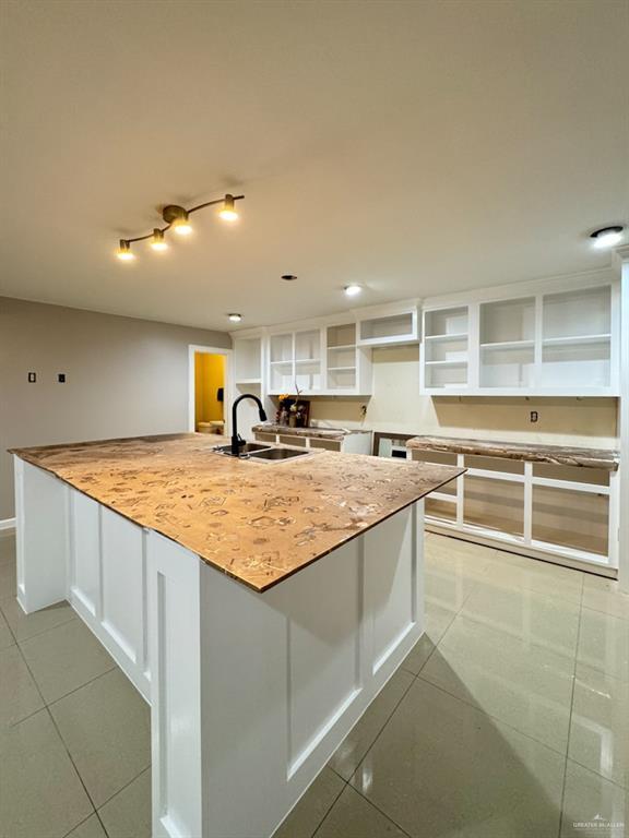 kitchen with light stone counters, light tile patterned floors, sink, and white cabinets