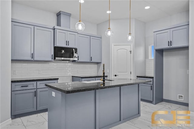 kitchen with tasteful backsplash, dark stone counters, an island with sink, and pendant lighting