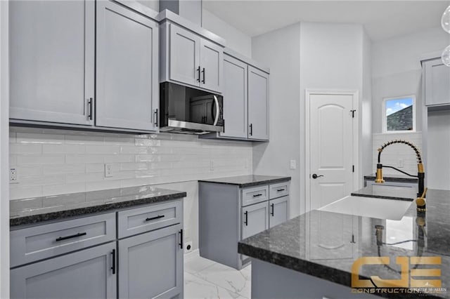 kitchen featuring decorative backsplash, gray cabinets, and dark stone counters