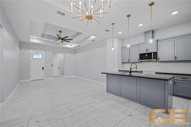 kitchen with gray cabinetry, a center island with sink, ceiling fan with notable chandelier, sink, and hanging light fixtures