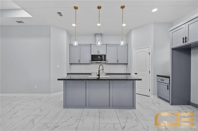 kitchen with a kitchen island with sink, dark stone counters, sink, gray cabinets, and decorative light fixtures