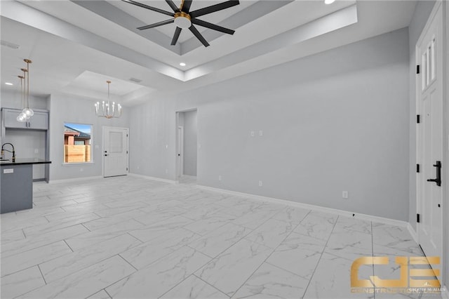 unfurnished living room featuring ceiling fan with notable chandelier, a tray ceiling, and sink