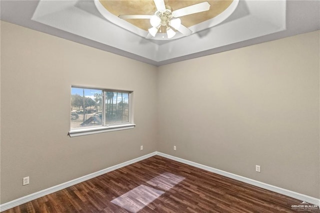 unfurnished room featuring ceiling fan, dark wood-type flooring, and a tray ceiling