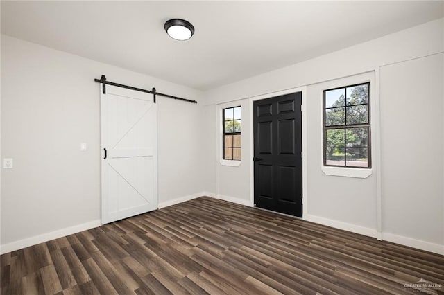 unfurnished room with a barn door, dark hardwood / wood-style floors, and a wealth of natural light